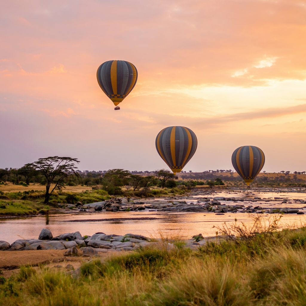 3 hot air balloons at sunrise over a gentle river in the Serengeti, Tanzania
