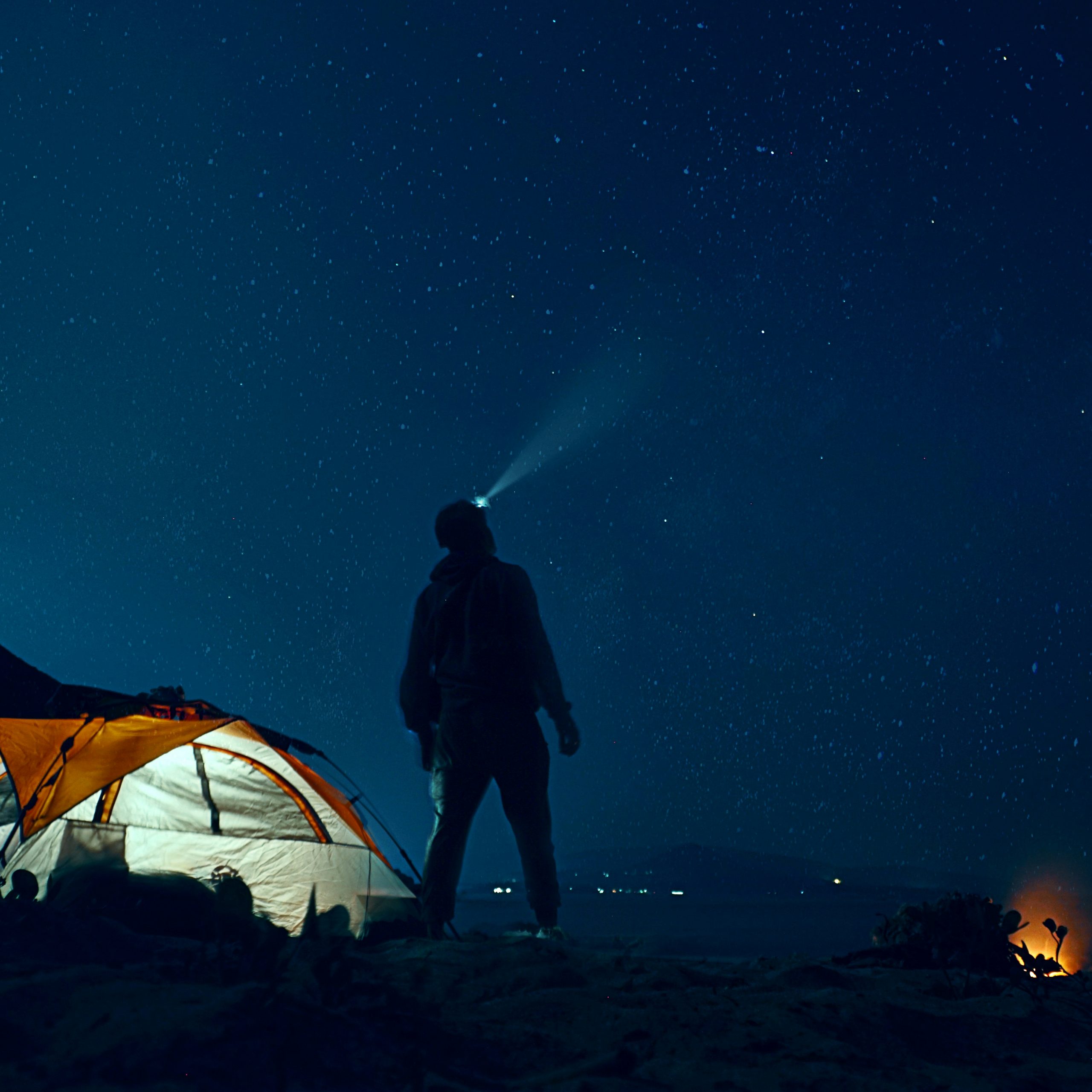 Man wearing a headlampo by his tent and looking at stars