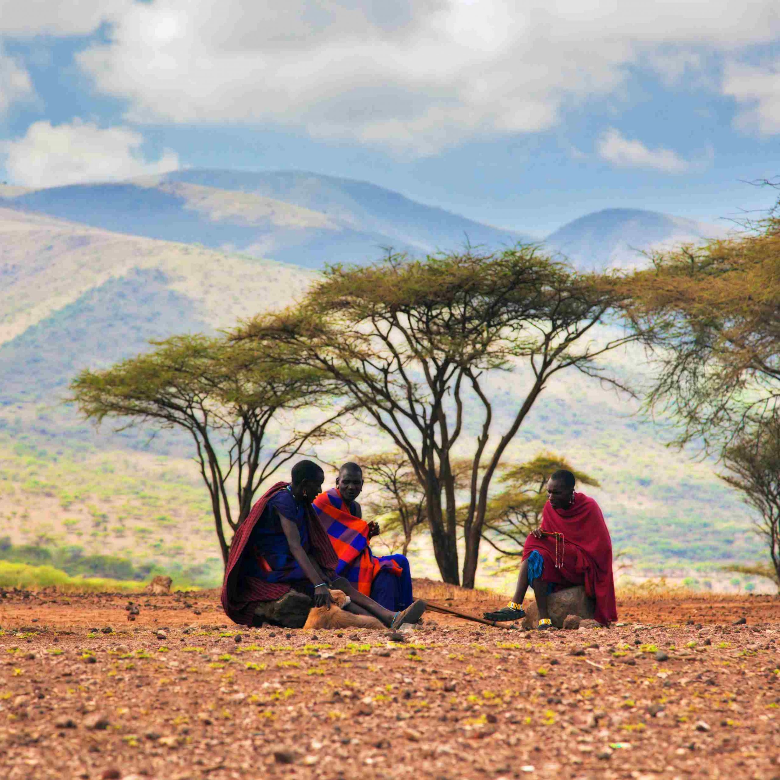 3 maasai warriors sitting in an open plain doing beadwork