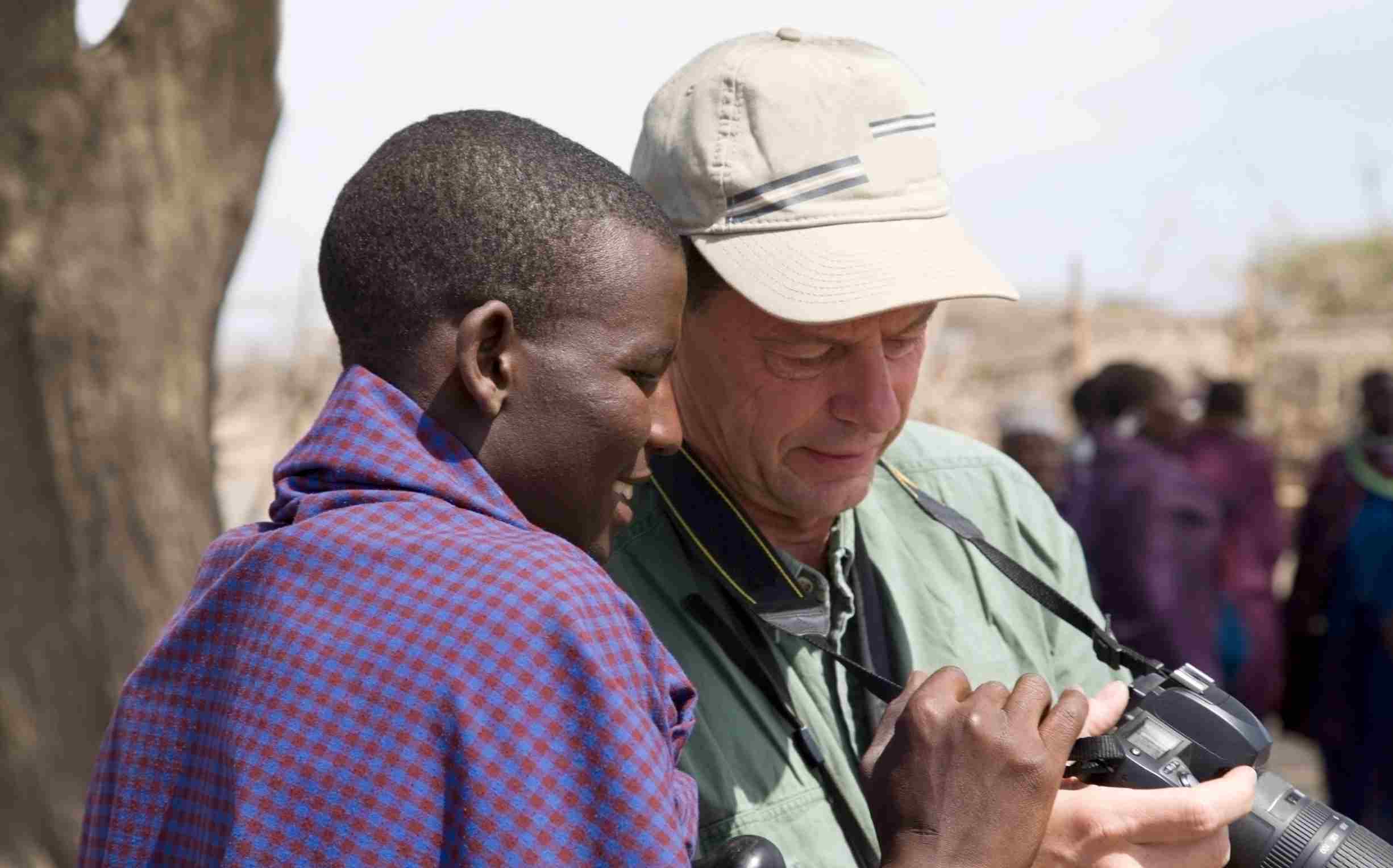 a young maasai man with a tourist looking at images on a camera