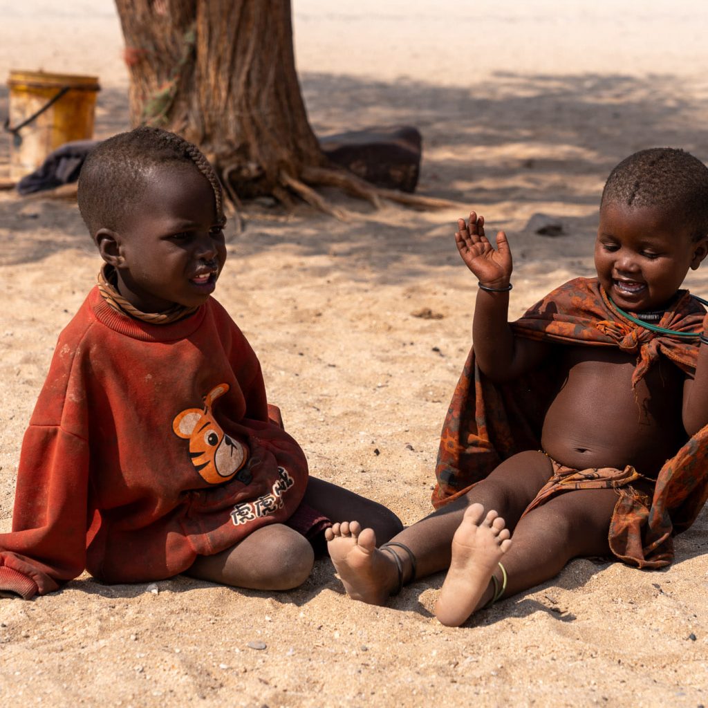 Himba toddlers seated on ground in sand, Namibia
