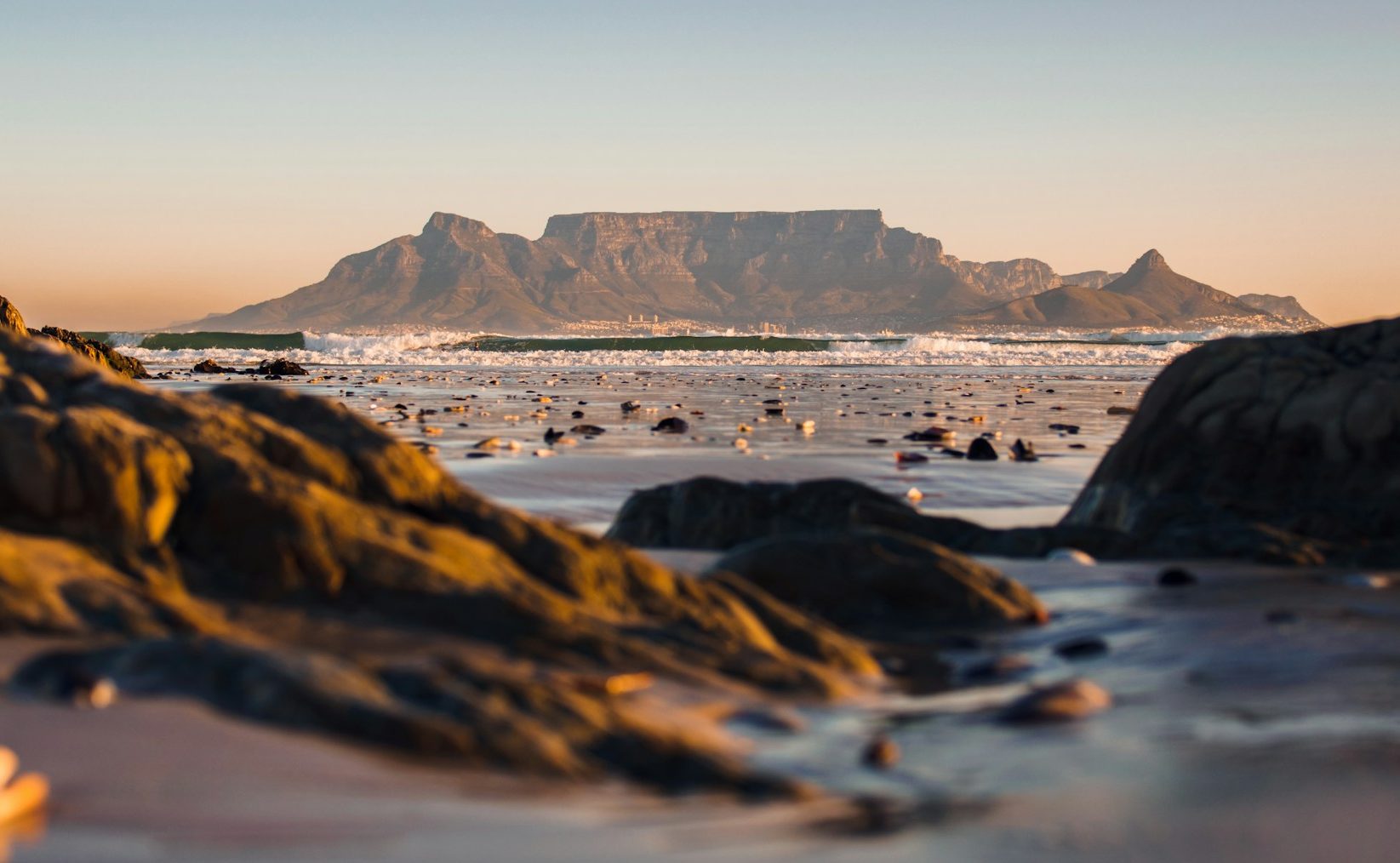 Table Mountain as seen from Blouberg Beach with sand and rocks of beach large ion foregrond from very low angle