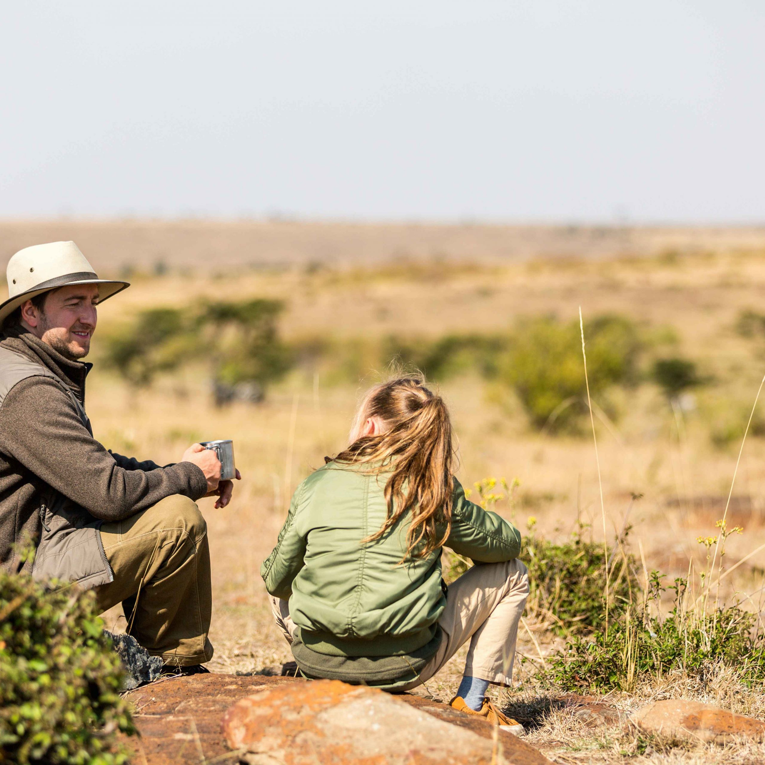 Father and daughter seated on rock in savannah, African safari