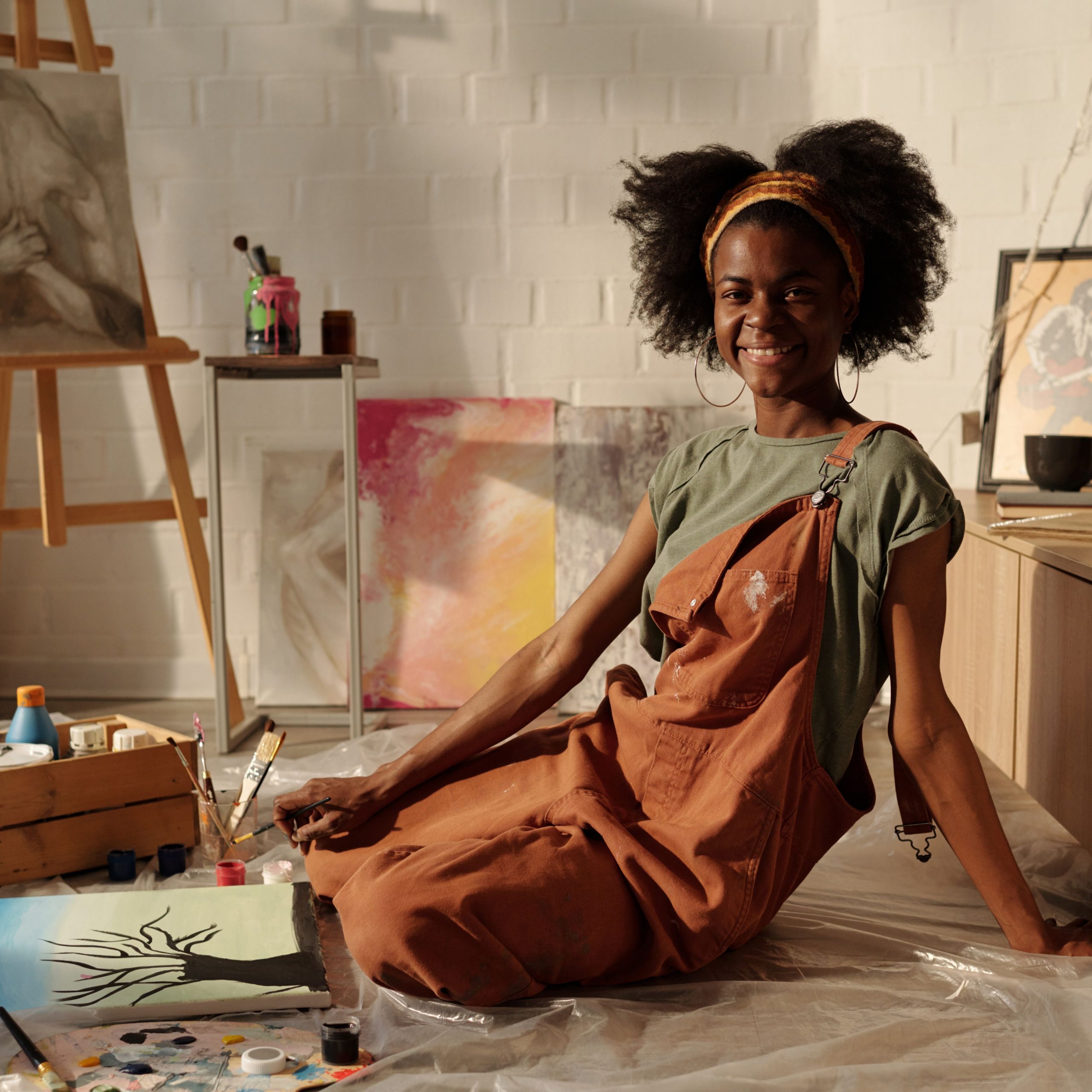 smiling-artist-sitting-in-art-studio-surrounded-by-paintings