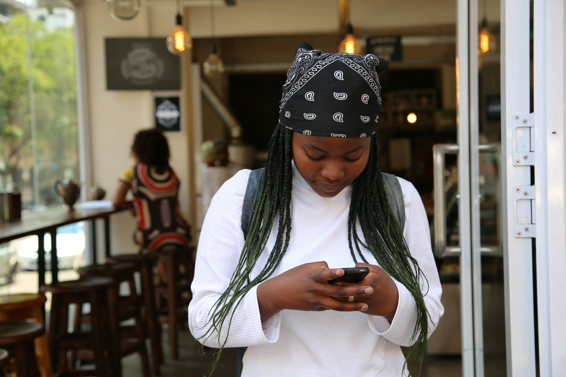 African girl outside cafe looking at smartphone