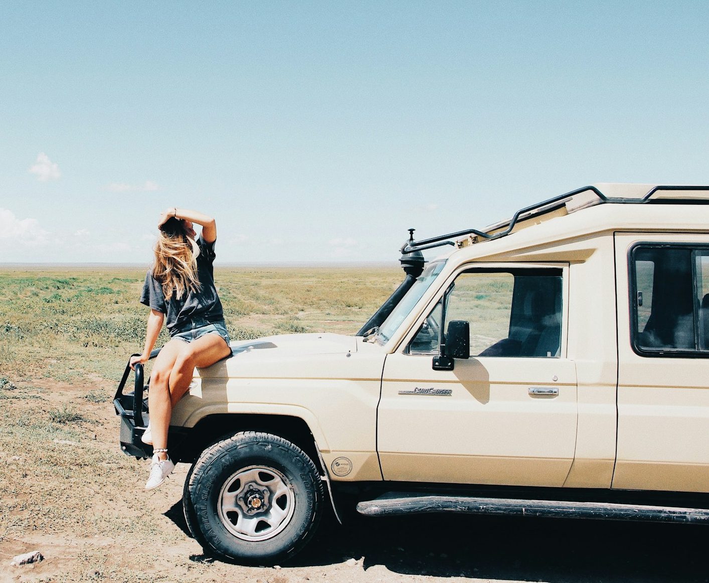 Female sitting on safari vehicle hood in open grassland