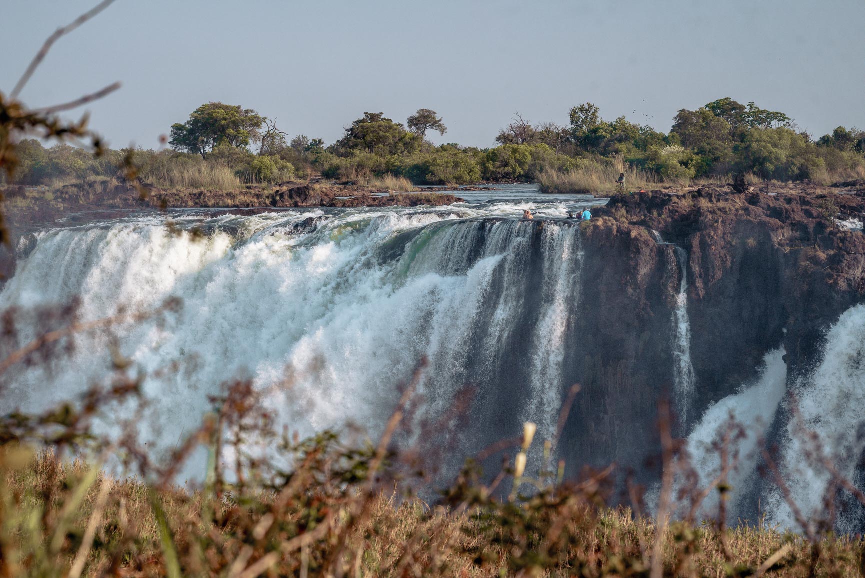 Victoria Falls seen from Zimbabwean side with swimmers in pools at top of falls