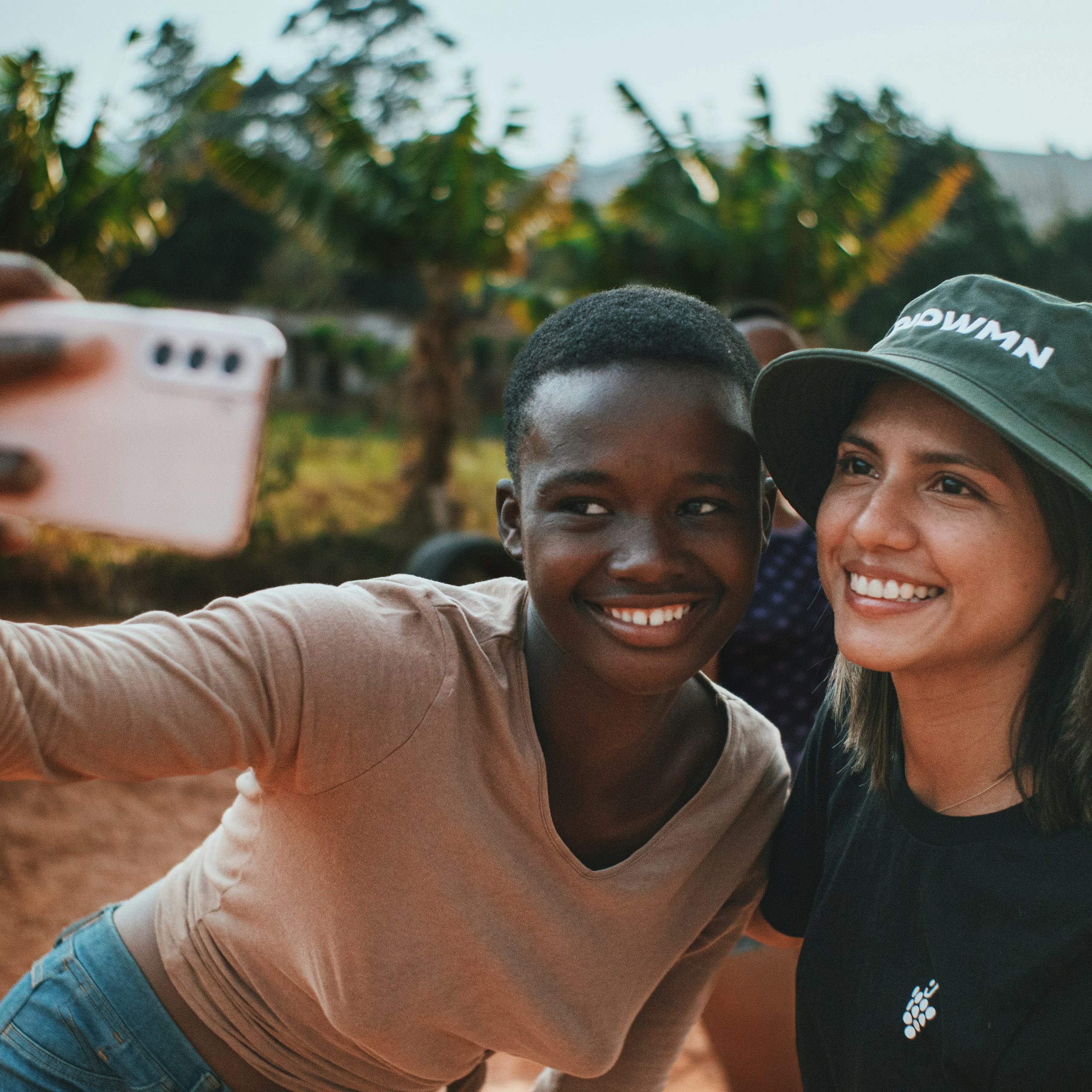 Young African girl and volunteer in a sunhat smiling together for a selfie in a rural setting in Africa