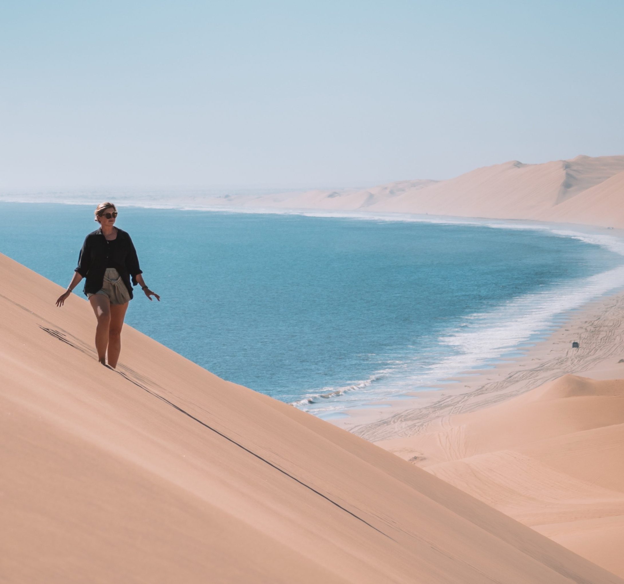 Woman walking on sand dune by coast, Skeleton Coast, Namibia safari