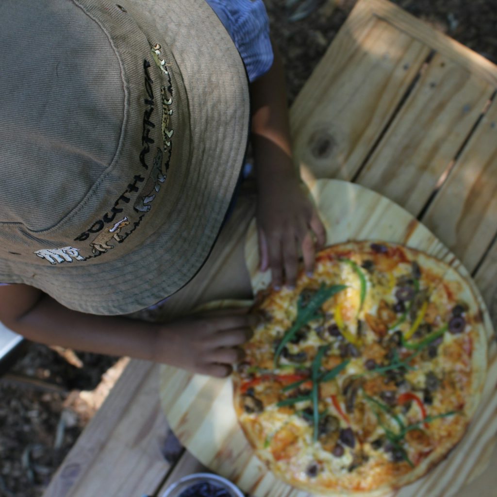 View from above of hatted individual with a pizza