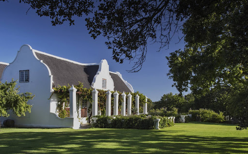 Historic Cape Dutch building at Meerlust Wine Estate, surrounded by lush lawns, trees, and vineyards in Stellenbosch. 