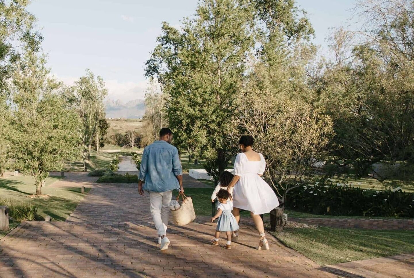 Family walking hand-in-hand in the beautiful gardens of Spier, Stellenbosch, towards a picnic spot on the wine farm.
