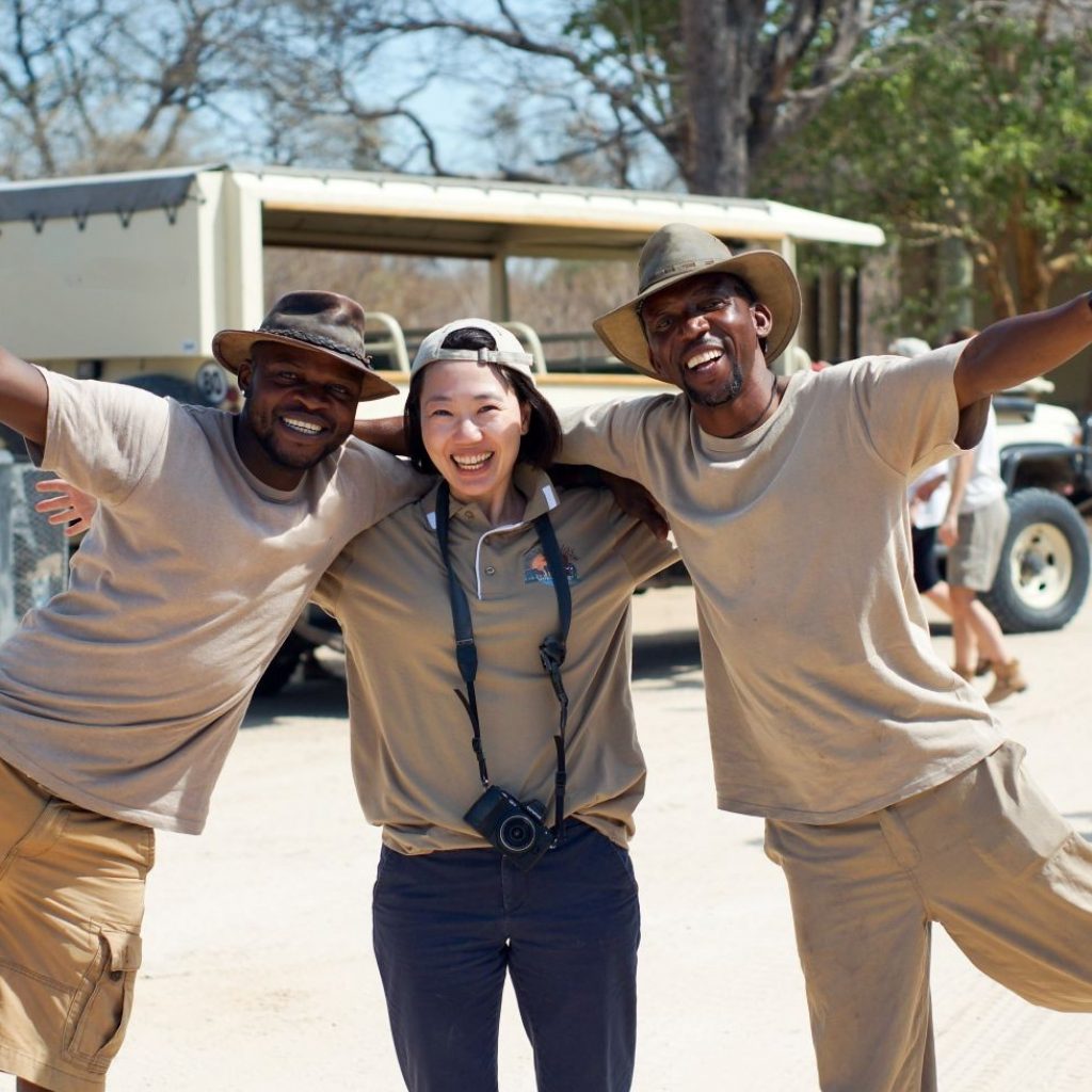 A female solo traveler happily posing with two safari guides in Namibia, emphasizing safety and companionship on a guided overland tour.