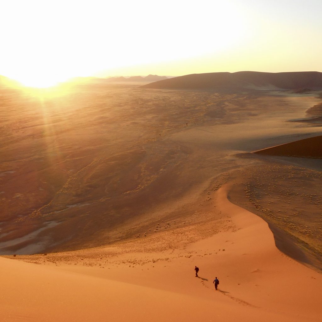People walking up steep sand dune in Namibia