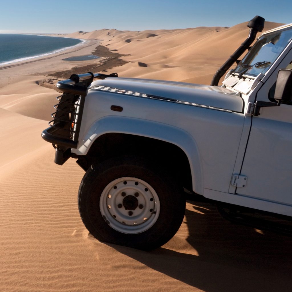4x4 on top of sand dune overlooking beach, Namib Desert, Namibia