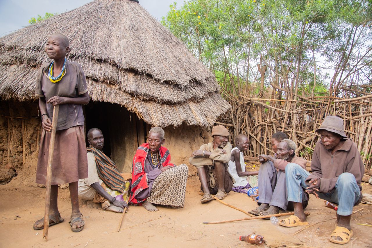 Maasai village elderly folks seated in front of thatched mud hut and cattle fence